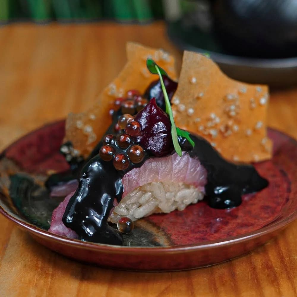 NIGIRI CON PESCA DEL DIA, SALSA ACEVICHADO, GEL DE HIBISCUS, IKURA, CROCANTE DE CAMOTE UN ESTALLIDO DE SABORES.